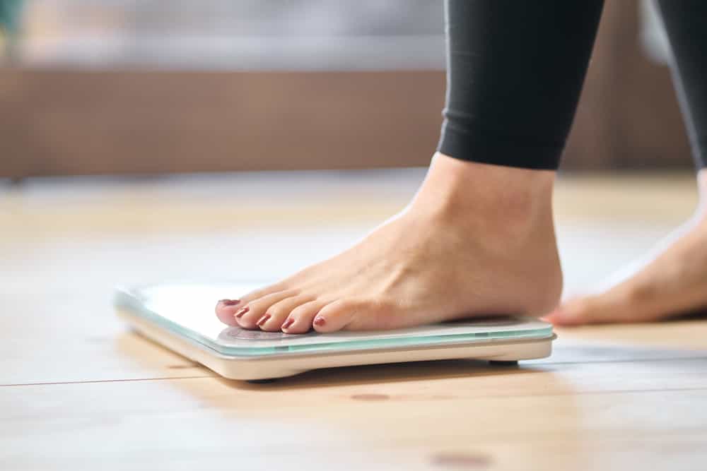 Woman weighing herself on a scale while tracking progress on how to lose 10 pounds in 2 weeks without exercise